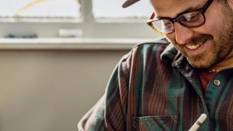 Image of the artist wearing a flannel and hat and drawing on a tablet.